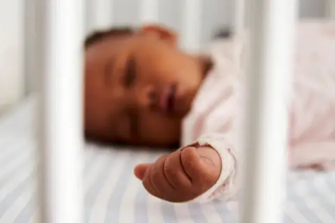 Ein Baby zuckt im Schlaf, seine kleine Hand liegt auf gestreifter Bettwäsche.