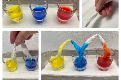 Krippe-Kinder experimentieren mit Farben: Papierstreifen saugen gelbe, blaue und rote Flüssigkeit auf und mischen sich.