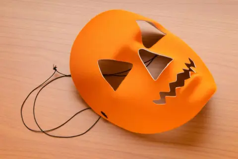 Orange halloween maske basteln: Kürbisgesicht mit Zackenmund und dreieckigen Augen auf Holzhintergrund.