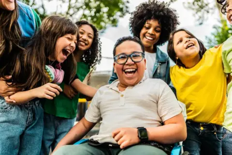 Fröhliche Kinder lachen und umarmen sich. Ein Junge im Rollstuhl strahlt. Wann ist Weltkindertag? An diesem Tag feiern wir alle Kinder!