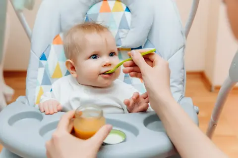 Ein süßes Baby von 6 Monaten sitzt im Hochstuhl und bekommt Brei gefüttert.