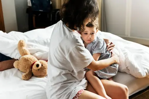 Mutter tröstet ihr Kind, das eine panikattacke hat. Ein Teddybär liegt daneben.