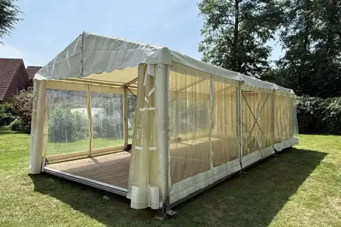 Ein Festzelt im Garten, bereit für eine Einschulungsfeier. Transparente Seitenwände lassen viel Licht herein.