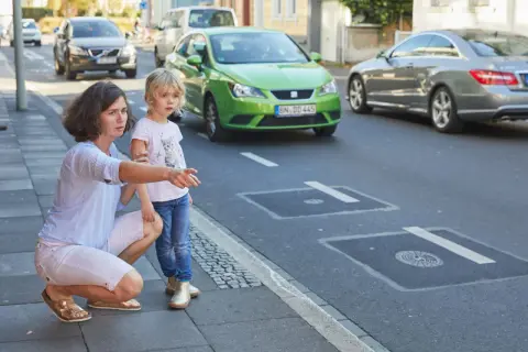 Frau erklärt Kind Verkehrsregeln am Zebrastreifen. Verkehrserziehung im Kindergarten ist wichtig.