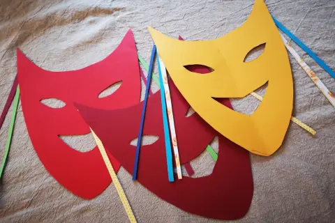 Bunte Karneval Maske Vorlagen liegen auf Stoff. Rot, dunkelrot und gelb. Bänder in verschiedenen Farben stecken an den Masken.