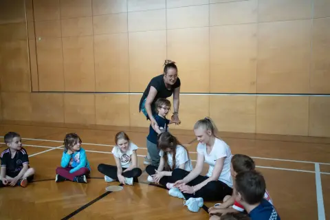 Lehrerin fördert die psychomotorik kinder in der Turnhalle. Kinder sitzen auf dem Boden und hören aufmerksam zu.