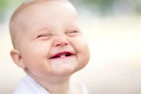 Ein Baby lacht herzhaft, die Augen geschlossen, die Wangen gerötet. Ab wann Babys laut lachen, ist oft eine Überraschung!
