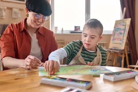 Lehrerin unterstützt Jungen mit Down-Syndrom beim Malen. Erste Eindrücke für die Eingangsdiagnostik Grundschule.