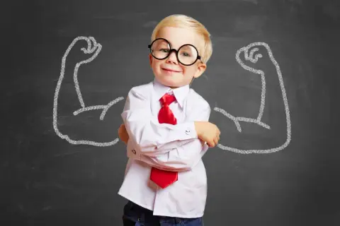 Kleiner Junge mit Brille und Krawatte, selbstbewusst vor Kreidezeichnungen starker Arme. So bekommt mein Kind mehr Selbstbewusstsein.