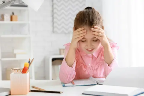 Ein Mädchen mit Händen an der Stirn, das über seinen Büchern sitzt. Die **Stress Kinder** sind deutlich zu sehen.