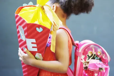 Ein Mädchen feiert die Einschulung mit einer bunten Zuckertüte und einem Rucksack mit Frozen-Motiv.