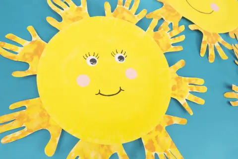 Süße Sonnen-Bastelarbeit von Kindern: Gelbe Pappteller-Sonnen mit Handabdruck-Strahlen und fröhlichen Gesichtern.