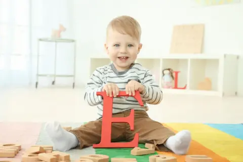 Ein lächelnder Junge hält den roten Buchstaben "E". Vielleicht ein zukünftiger Elias oder Emil, einer der vielen Jungennamen mit E.