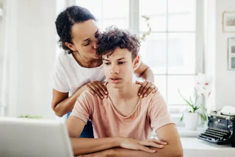 Mutter küsst Sohn auf die Stirn, legt Hände auf seine Schultern. Sie liebt ein narzisst seine Kinder, doch hier wirkt es wie echte Zuneigung.