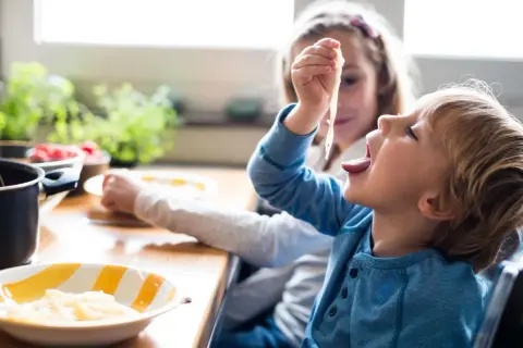 Große Schwester versucht, den kleinen Bruder zum Essen zu überreden, der nicht essen will.
