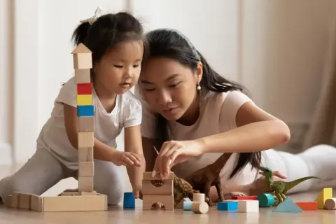 Mutter und Kind bauen mit Holzklötzen und Dinosauriern. Feinmotorik Kinder wird spielerisch gefördert.