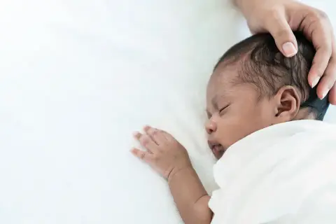 Ein süßes Baby schwitzt beim Schlafen am Kopf. Eine Hand streichelt sanft über das dunkle Haar.