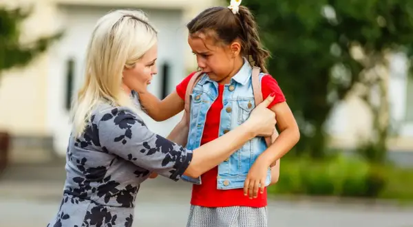 Mutter tröstet weinendes Kind mit Trennungsangst vor der Schule.