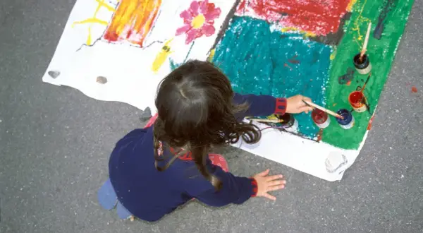 Ein Kind malt auf einem großen Blatt Papier. Die bunten Farben und die Art der Zeichnung könnten auf die Verarbeitung von kinderzeichnungen trauma hindeuten.