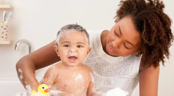 Mutter wäscht ihr Baby mit Schaum und Quietscheente. Ein warmes Bad kann bei Fieber helfen.