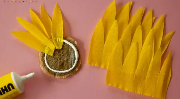 Sonnenblume basteln Krippe: Gelbe Blütenblätter aus Krepppapier werden auf einen Teebeutel geklebt.