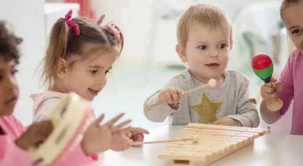 Kinder haben Spaß mit Musik im Kindergarten. Sie spielen Xylophon, Tamburin und Maracas.