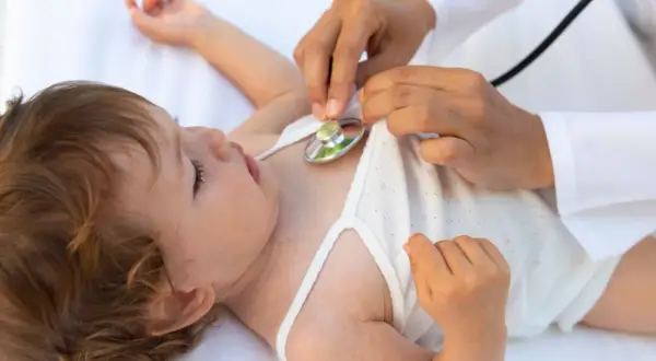 Arzt hört mit Stethoskop auf das Herz eines Babys. Eine U6 Untersuchung ist wichtig für die Gesundheit des Kindes.