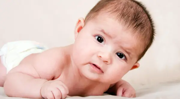 Ein süßes Baby, 4 Wochen alt, liegt auf dem Bauch und blickt neugierig in die Kamera.