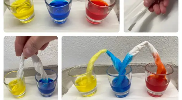 Krippe-Kinder experimentieren mit Farben: Papierstreifen saugen gelbe, blaue und rote Flüssigkeit auf und mischen sich.