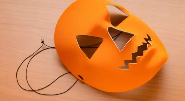 Orange halloween maske basteln: Kürbisgesicht mit Zackenmund und dreieckigen Augen auf Holzhintergrund.