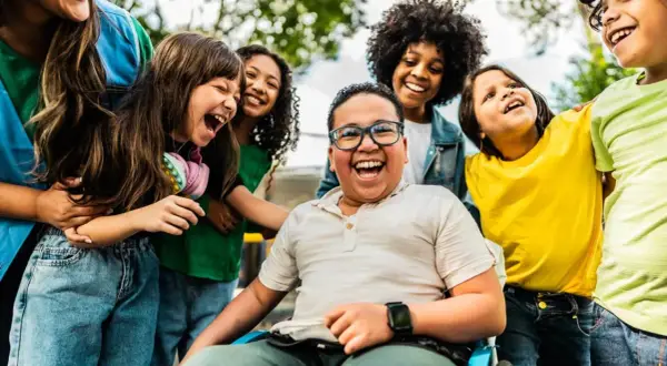 Fröhliche Kinder lachen und umarmen sich. Ein Junge im Rollstuhl strahlt. Wann ist Weltkindertag? An diesem Tag feiern wir alle Kinder!