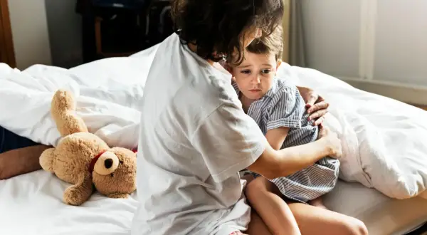 Mutter tröstet ihr Kind, das eine panikattacke hat. Ein Teddybär liegt daneben.
