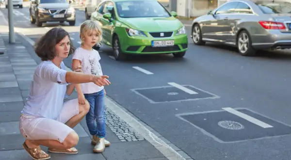 Frau erklärt Kind Verkehrsregeln am Zebrastreifen. Verkehrserziehung im Kindergarten ist wichtig.