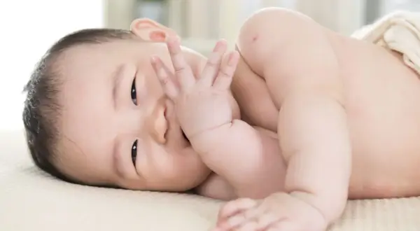 Ein süßer **baby 11 wochen** alt liegt auf der Seite und bedeckt seinen Mund mit der Hand.