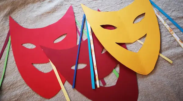 Bunte Karneval Maske Vorlagen liegen auf Stoff. Rot, dunkelrot und gelb. Bänder in verschiedenen Farben stecken an den Masken.