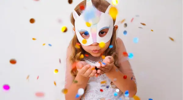 Kind mit Einhorn-Maske pustet Konfetti. Perfekt für Ideen zum Masken basteln, Vorlagen ausdrucken und eine magische Feier.
