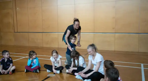 Lehrerin fördert die psychomotorik kinder in der Turnhalle. Kinder sitzen auf dem Boden und hören aufmerksam zu.