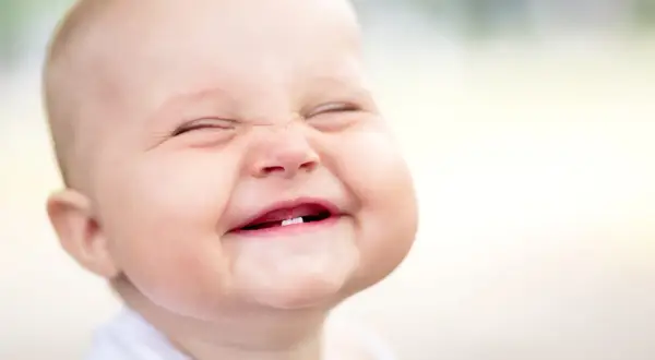 Ein Baby lacht herzhaft, die Augen geschlossen, die Wangen gerötet. Ab wann Babys laut lachen, ist oft eine Überraschung!