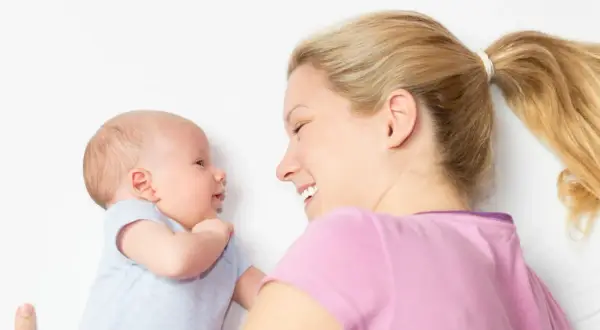 Ein lächelnder baby 2 wochen alt schaut seine Mutter an. Sie liegt neben ihm und lächelt zurück.