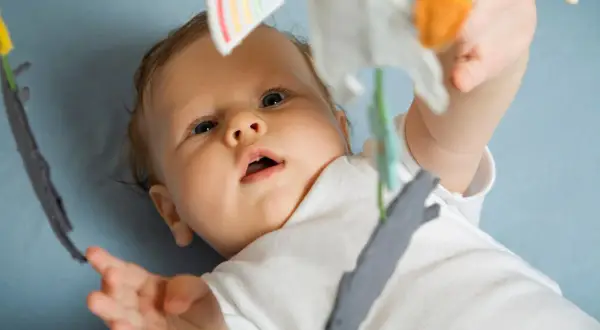 Ein neugieriges Baby, 15 Wochen alt, streckt seine Hand nach einem Spielzeug aus.