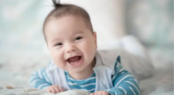 Ein fröhliches Baby, 21 Wochen alt, liegt auf dem Bauch und lacht herzhaft.