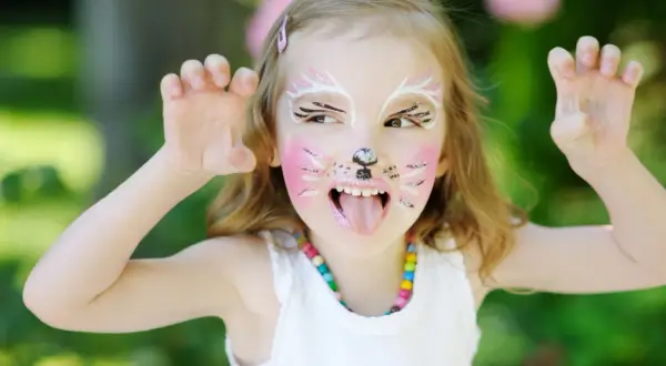 Ein Kind mit süßem Katzen-Make-up, das mit den Pfoten nach oben zeigt. Das Kind hat rosa Wangen, Schnurrhaare und eine schwarze Nase.