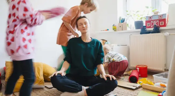 Mama Burnout? Sie meditiert inmitten des Chaos ihrer Kinder. Ein Moment der Ruhe, um Kraft zu tanken.