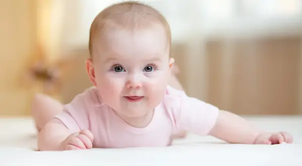 Ein süßes Baby mit blauen Augen liegt auf dem Bauch und versucht, den Kopf zu halten. Es trägt ein rosa Body.