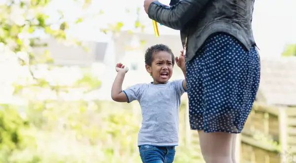 Ein 3-jähriger Junge schreit und hält die Arme hoch, während eine Frau Seifenblasen macht. Ein Moment der Entwicklung.