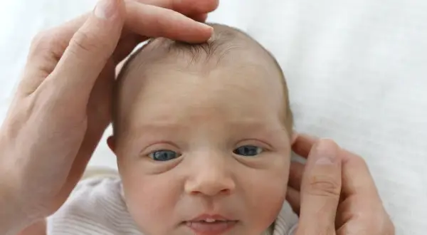 Sanft berühren die Hände eines Elternteils das Köpfchen eines Babys. Die Fontanelle ist leicht eingefallen, ein Zeichen für mögliche Dehydrierung.