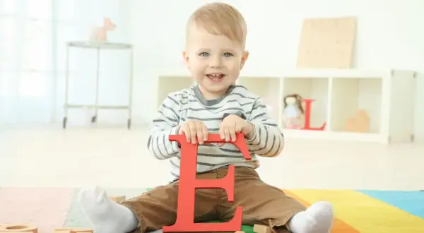 Ein lächelnder Junge hält den roten Buchstaben "E". Vielleicht ein zukünftiger Elias oder Emil, einer der vielen Jungennamen mit E.