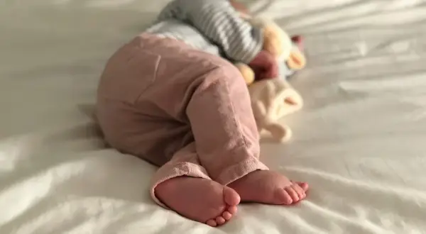 Ein Baby schläft auf einer weißen Decke, die Füße nach vorne gestreckt. Es ist ein Zeichen für einen Wachstumsschub, wenn Babys so tief und fest schlafen.