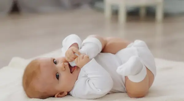 Ein süßes Baby, 8 Wochen alt, liegt auf einer weichen Decke und spielt mit seinen Füßen.