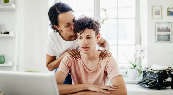 Mutter küsst Sohn auf die Stirn, legt Hände auf seine Schultern. Sie liebt ein narzisst seine Kinder, doch hier wirkt es wie echte Zuneigung.